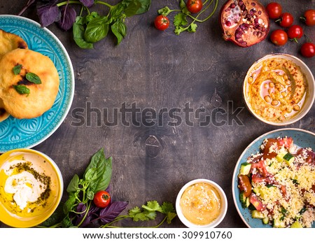 Table served with middle eastern traditional vegetarian dishes. Hummus, tahini, pitta, couscous salad and buttermilk dip with olive oil. Dinner party