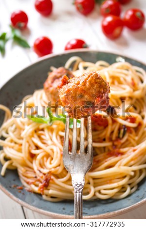 Close-up of delicious meatball on a fork. Spaghetti with meatballs and tomato sauce on a plate. Serving on a white rustic wooden table. An Italian-American dish. Selective focus