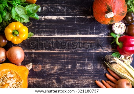 Fresh vegetables on a old dark textured table. Autumn background. Healthy eating frame. Sliced pumpkin, bell peppers, carrots, onions, cut garlic, tomatoes, rucola and basil. Top view. Space for text