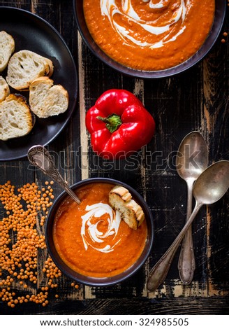 Delicious pumpkin soup with heavy cream on dark rustic wooden table with red bell pepper, bread toasts, lentil. Top view