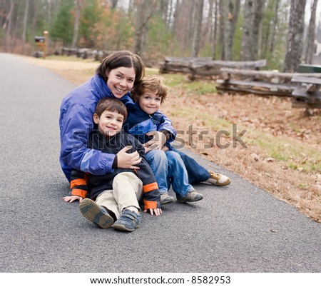 Thirtysomething mom sitting in driveway with preschool sons in winter.