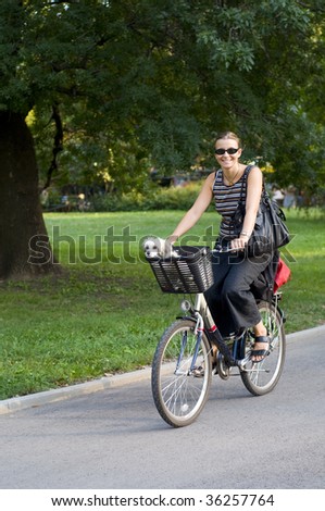 Woman on bicycle smiling with her white dog in a basket on the bike.