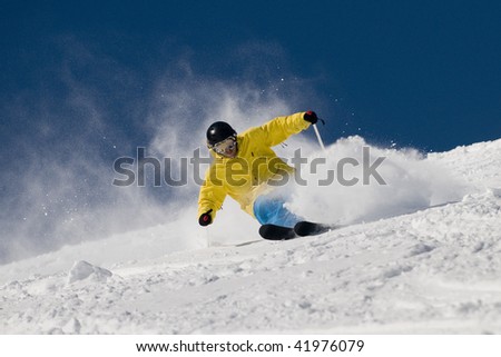 Skier moving down on ski slope against blue sky.