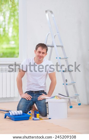 young man painter sittin on the floor with painting tools and looking at camera smiling