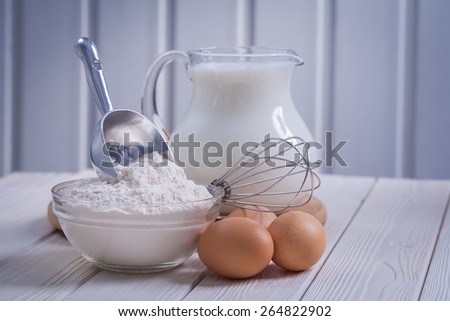 composition of kitchen objects eggs bowl with flour pitcher milk on white painted old wooden board food and drink concept