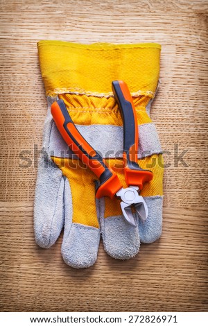 classical nippers and protective working glove on wooden board construction concept
