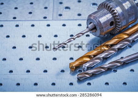 Steel drill with boring bits on perforated metallic background construction concept.