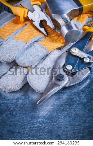Safety gloves with claw hammer pliers and tin snips on scratched metallic background construction concept.
