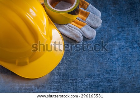 Safety tape yellow building helmet and protective gloves on scratched vintage metallic background construction concept.