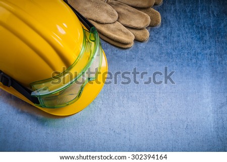 Group of safety working gloves hard hat and transparent protective glasses on scratched metallic background construction concept.