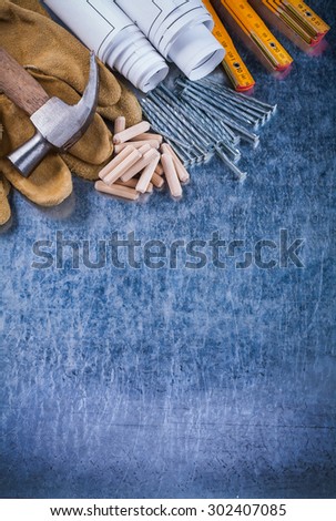 Construction plans claw hammer safety gloves wooden meter metal nails and dowels on scratched metallic surface maintenance concept.
