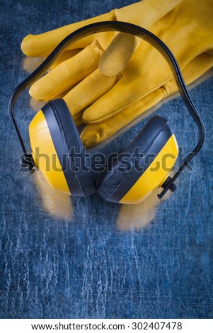 Noise reduction yellow headphones and leather safety gloves on scratched metallic background construction concept.