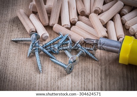 Wooden dowels construction nails and insulated screwdriver on wood board.