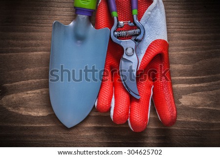 Protective glove garden pruner and shovel on wooden board.