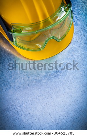 Copy space of yellow hard hat with multiple-purpose protective glasses on scratched metallic background construction concept.
