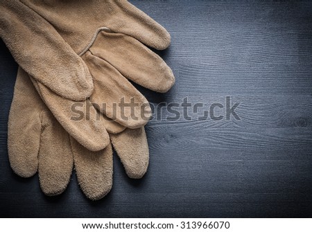 two working leather gloves on dark wood board.