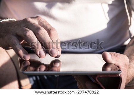 Scrolling on a modern digital tablet outdoor. Close up. Focus on the hands. Slight desaturated filtered look.