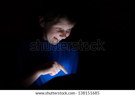young boy using an electronic tablet device with finger pointing. Light coming from the tablet