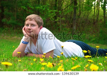 handsome teenager boy laying down in a field of yellow dandelion flowers smiling at the viewer
