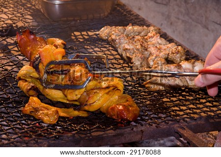 pork fillet and chicken kebabs being grilled on an open fire and being turned by hand with tongs