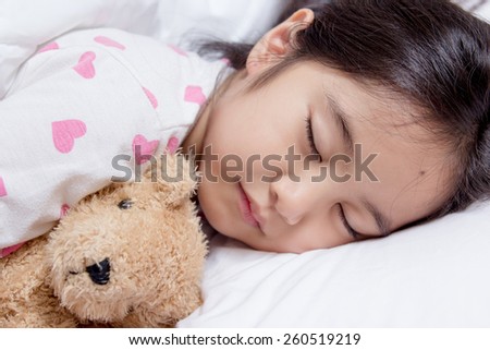 Adorable little Asian girl sleep on her bed with bear doll