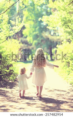 Sunny photo two little sisters holding hands walking barefoot in the forest on a summer day