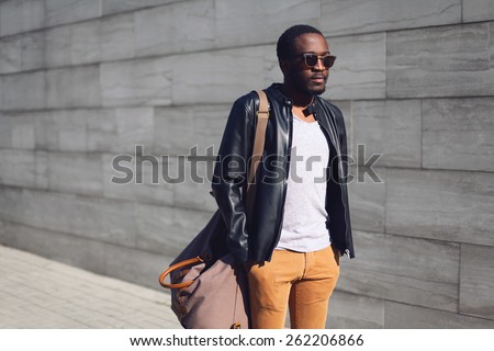 Street fashion concept - stylish handsome african man standing in the city against a gray textured wall