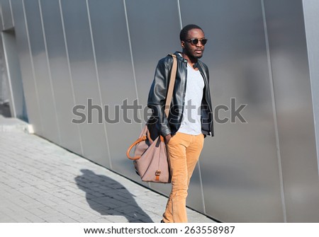 Street fashion concept - handsome stylish young african man walks evening in the city against a urban building wall
