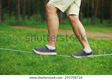 Sport, leisure, recreation and healthy lifestyle concept - man slacklining walking and balancing on a rope closeup legs, slackline in summer day