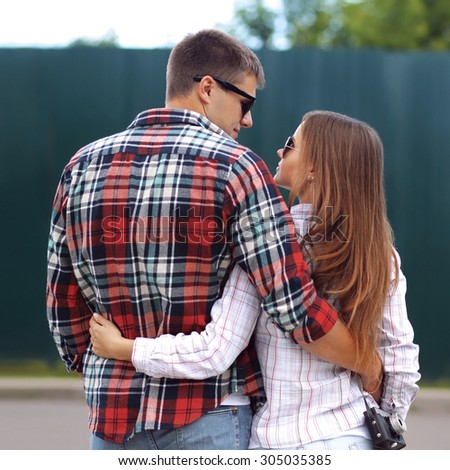 Young beautiful sweet couple hugging in the city, wearing checkered shirts and sunglasses, view back