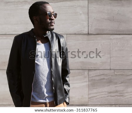 Fashion portrait of stylish young african man wearing a sunglasses and black rock leather jacket over textured background