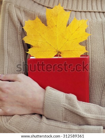 Female hands holding book with autumn yellow maple leaf close-up