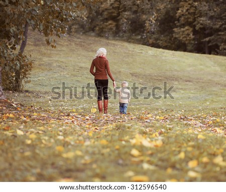 Mother and child walking together in autumn park, life moment