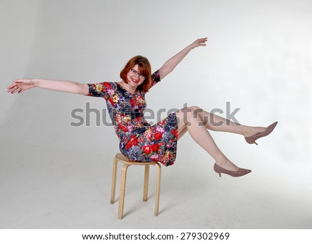 Funny smiling red haired woman in glasses sitting on stool