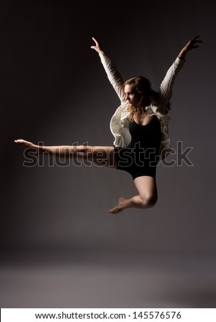 Beautiful slim young female modern jazz contemporary style ballet dancer wearing a black leotard and white shirt on a neutral grey studio background