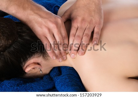 Adult male physiotherapist treating the back of a female patient. Patient is lying down on a bed and is covered with royal blue towels.