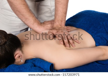 Adult male physiotherapist treating the back of a female patient. Patient is lying down on a bed and is covered with royal blue towels.