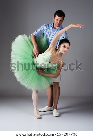 Beautiful female ballet dancer and dance teacher on a grey background. Ballerina is wearing a green tutu and pointe shoes. Instructor in plain clothes.