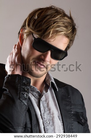 Portrait of a handsome blonde caucasian man wearing a faded blue button shirt, black jacket with leather and sunglasses.