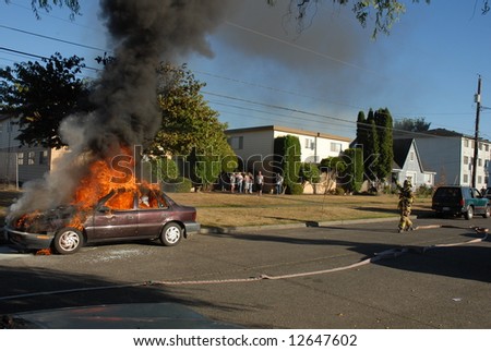 A car caught on fire in the street and firefighters work on putting out the fire.