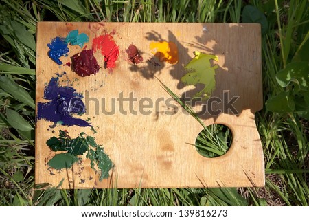 Background with a wood palette with oil paint lying on the grass