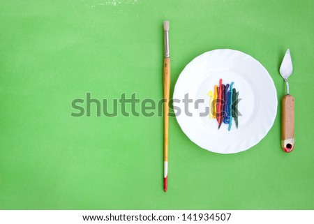 Artistic bright green background with oil paint on a white plate and painting instruments served like a dish