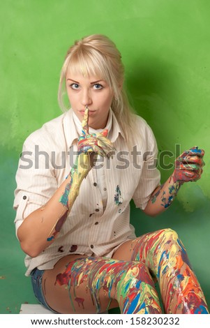 Attractive woman with hands and legs covered with paint makes a hush and secret gesture