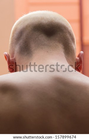 Head or neck of young man with shaved head looking out a window overlooking the back