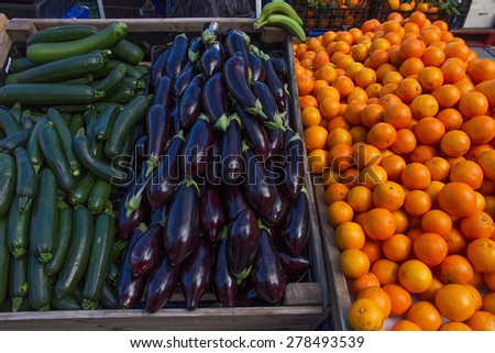 Expose for sale at a market stall, outdoors, with fruits and vegetables (oranges, aubergines, courgettes, bananas, Different types of beans or beans arranged in sacks for sale in the market