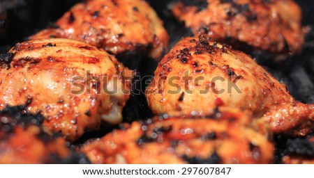 Grilled chicken thighs on a charcoal barbecue grill being cooked with seasoning and sauce