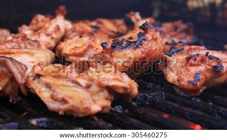 Mouth watering chicken thighs being grilled on cast iron grates over charcoal with smoke and flames