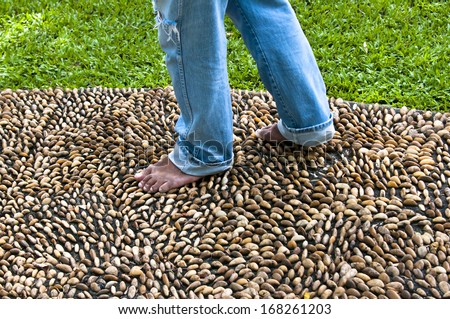 A man walking on stone for foot massage - pebble on cement path - walk therapy relaxation treatment ache