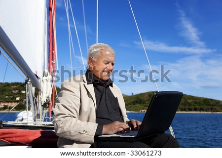 The businessman is working during the vacation on a sailboat with a lovely beach in the background.