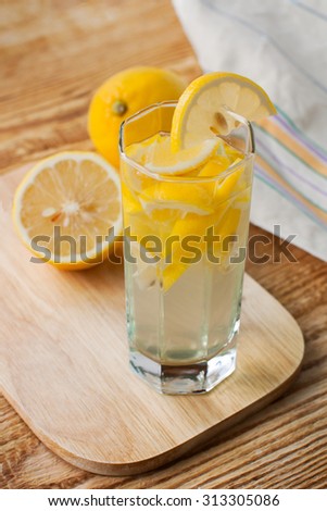Home refreshing lemonade delicious - sweet drink of lemon in a glass transparent glass on a cutting board and wooden table, rustic style.
